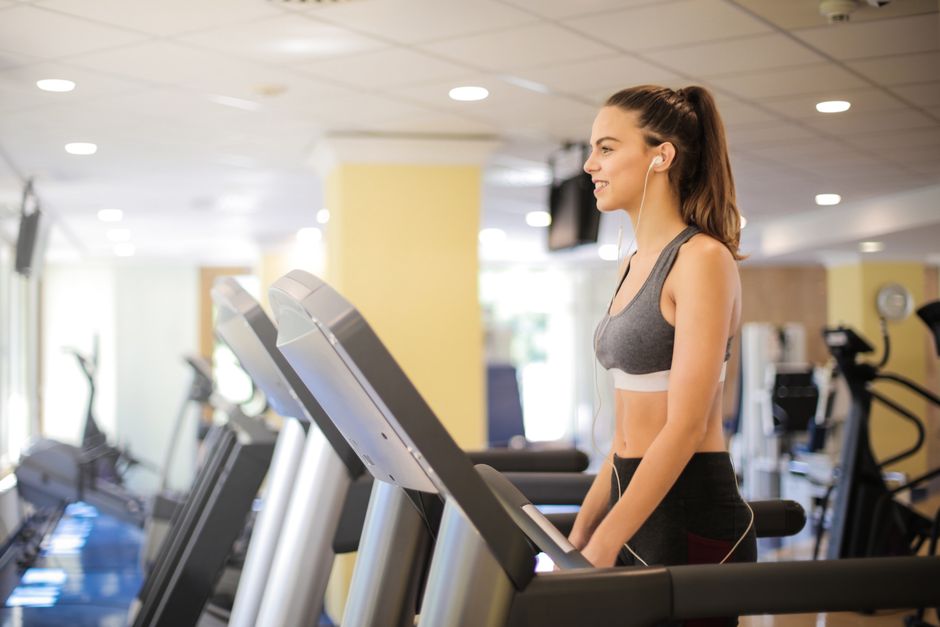 Jovem mulher treinando na esteira enquanto se exercita em academia moderna, demonstrando bem-estar e atividade física.